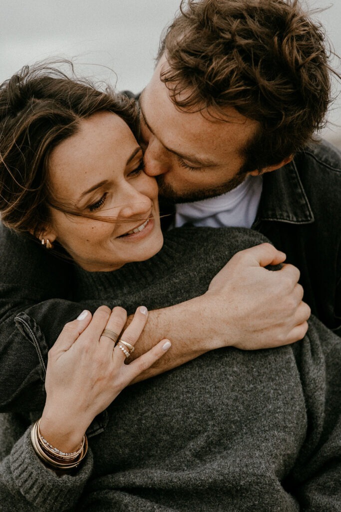 gros plan sur les futurs parents qui s'enlacent pendant leur séance photo à la plage l'hiver à montpellier