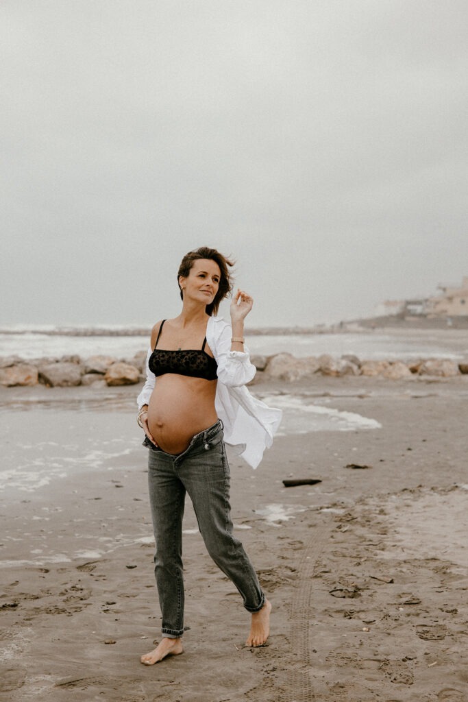 future maman qui marche au bord de l'eau pour sa séance photo grossesse l'hiver à la plage