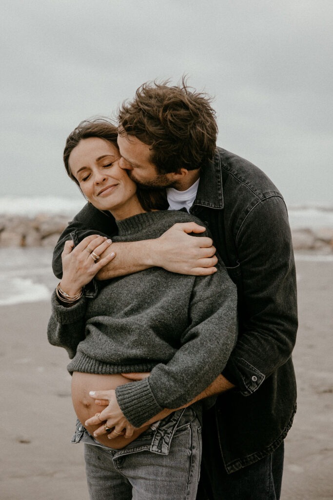 gros plan sur les futurs parents qui s'enlacent pendant leur séance photo à la plage l'hiver à montpellier